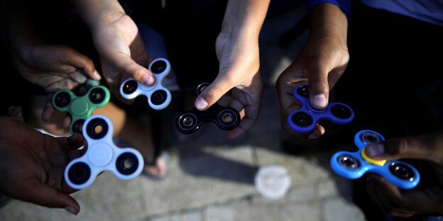 Man sieht die Hände von drei Kindern, die jeweils zwei Fidget Spinner halten. Man sieht die Hände von drei Kindern, die jeweils zwei Fidget Spinner halten.