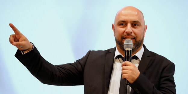 ein Mann mit Mikrofon, den rechten Arm und Zeigefinger ausgestreckt ein Mann mit Mikrofon, den rechten Arm und Zeigefinger ausgestreckt
