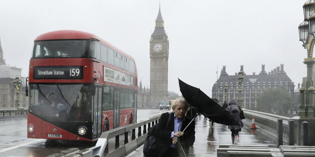 Ein Mann mit einem Regenschirm geht am 06.06.2017 auf der Westminister Bridge in London (Großbritannien) im Regen entlang einer Absperrung, im Hintergrund ist ein roter Doppeldeckerbus zu sehen. Ein Mann mit einem Regenschirm geht am 06.06.2017 auf der Westminister Bridge in London (Großbritannien) im Regen entlang einer Absperrung, im Hintergrund ist ein roter Doppeldeckerbus zu sehen.