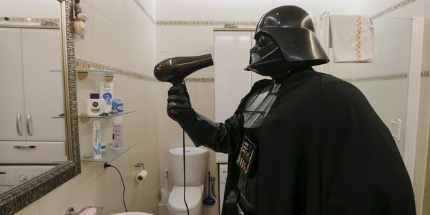 Ein Mann im Kostüm von Darth Vader hält einen Föhn Ein Mann im Kostüm von Darth Vader hält einen Föhn