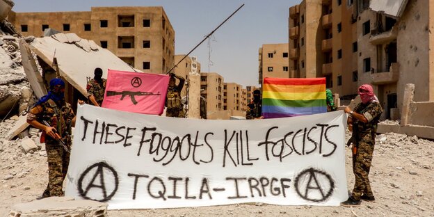 zwei Menschen in Tarnanzügen zeigen ein Transparent mit der Aufschrift "These faggits kill fascists", darüber eine Regenbogenfahne, dahinter eine halb zerstörte Stadt zwei Menschen in Tarnanzügen zeigen ein Transparent mit der Aufschrift "These faggits kill fascists", darüber eine Regenbogenfahne, dahinter eine halb zerstörte Stadt