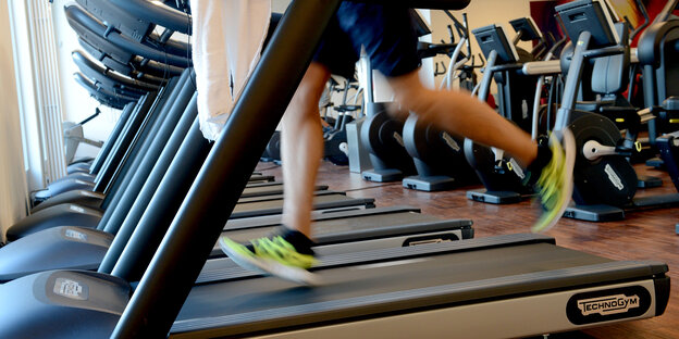 Fitnessstudio von innen. Viele Laufbänder nebeneinander, auf dem vordersten sieht man die Beinen eines weißen Sportlers. Fitnessstudio von innen. Viele Laufbänder nebeneinander, auf dem vordersten sieht man die Beinen eines weißen Sportlers.