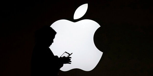 Die Silhouette einer Person vor einem Apple-Logo Die Silhouette einer Person vor einem Apple-Logo