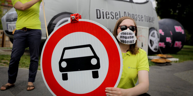 Eine Demonstrantin hält eine Verbotsschild für Autos hoch.