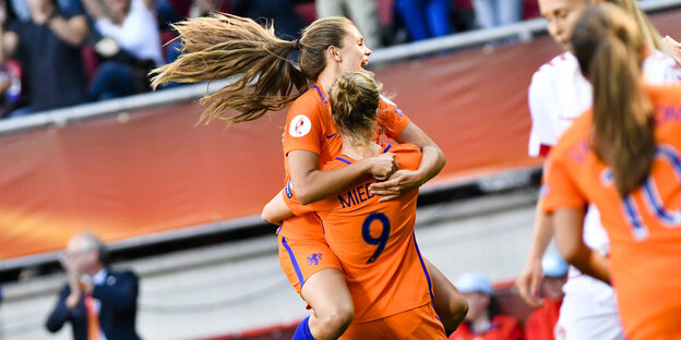 Zwei Frauen in orangefarbenen Fußballtrikots umarmen sich jubelnd Zwei Frauen in orangefarbenen Fußballtrikots umarmen sich jubelnd