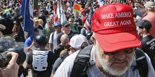 Ein Mann mit rotem "Make America Great Again"-Basecap vor einer Menschenmenge Ein Mann mit rotem "Make America Great Again"-Basecap vor einer Menschenmenge