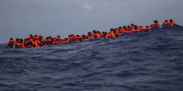 Migranten mit roten Schwimmwesten im Meer Migranten mit roten Schwimmwesten im Meer