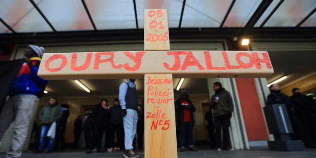 Auf einem Holzkreuz steht in roten Buchstaben der Name Oury Jallohs Auf einem Holzkreuz steht in roten Buchstaben der Name Oury Jallohs