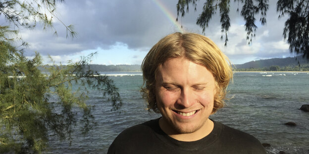 ein grinsender Mann am Ufer, hinter ihm ein Regenbogen ein grinsender Mann am Ufer, hinter ihm ein Regenbogen