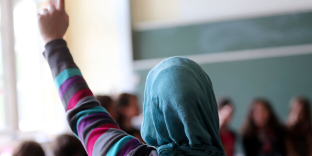 Eine Schülerin mit Kopftuch zeigt auf Eine Schülerin mit Kopftuch zeigt auf