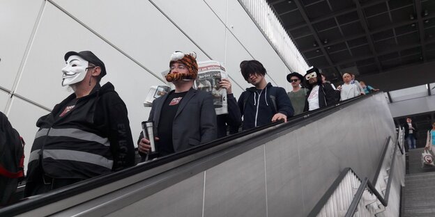 Menschen mit Masken fahren eine Rolltreppe herunter Menschen mit Masken fahren eine Rolltreppe herunter