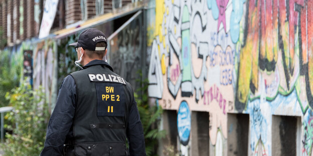 Ein Polizist in Montur läuft neben eine Hauswand, die mit Graffiti besprüht ist Ein Polizist in Montur läuft neben eine Hauswand, die mit Graffiti besprüht ist