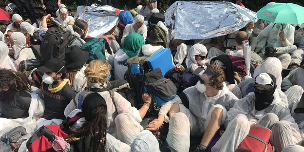 Menschen in weißer Schutzbekleidung sitzen dicht gedrängt am Boden Menschen in weißer Schutzbekleidung sitzen dicht gedrängt am Boden