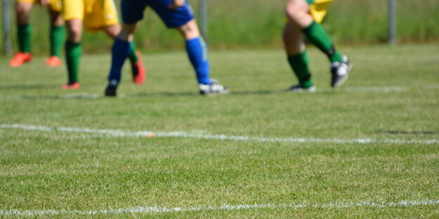 Rasen, im Hintergrund die Beine von Fußballspielern