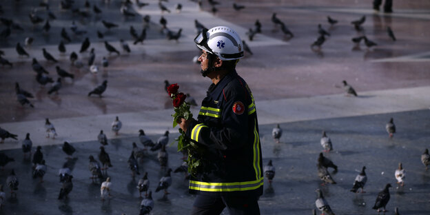 Ein Feuerwehrmann trägt Rosen über einen Platz voller Tauben Ein Feuerwehrmann trägt Rosen über einen Platz voller Tauben