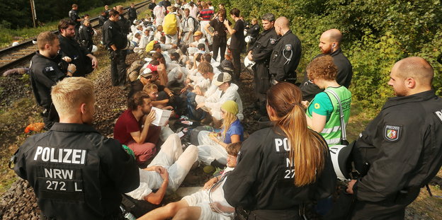 Menschen sitzen auf Gleisen. Davor einige Polizisten in Montur