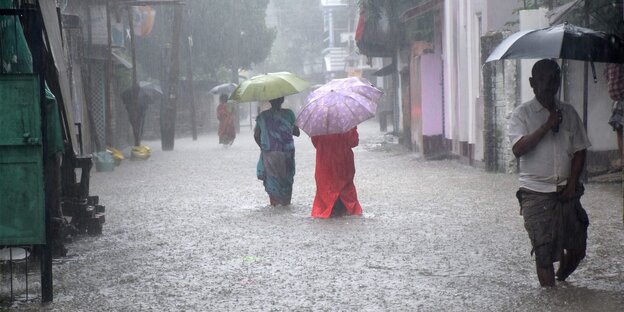 Menschen mit Regenschirm waten durch Wasser Menschen mit Regenschirm waten durch Wasser