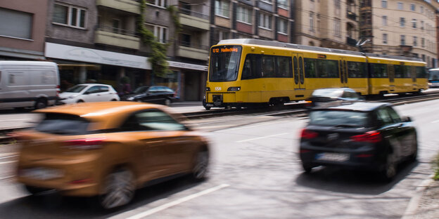 Eine gelbe Straßenbahn fährt in die linke Richtung, zwei durch die Bewegung verschwommene Autos davor in die Gegenrichtung Eine gelbe Straßenbahn fährt in die linke Richtung, zwei durch die Bewegung verschwommene Autos davor in die Gegenrichtung