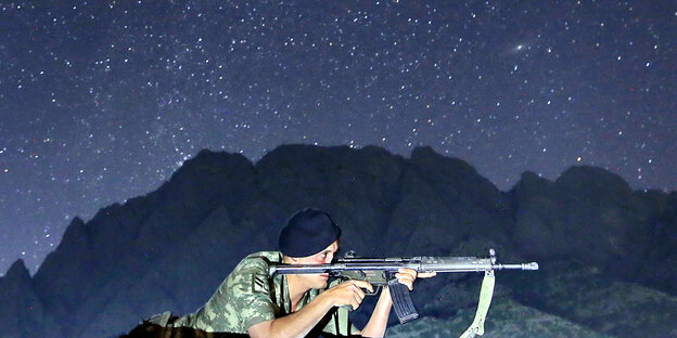 Ein Soldat liegt mit seinem Gewehr im Anschlag in einer hügeligen Landschaft unter einem Sternenhimmel Ein Soldat liegt mit seinem Gewehr im Anschlag in einer hügeligen Landschaft unter einem Sternenhimmel