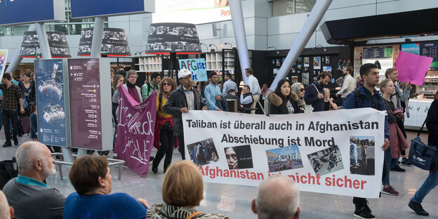 Menschen tragen Transparente durch eine Flughafenhalle