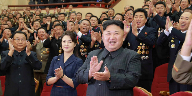 Kim Jong Un steht mit vielen Menschen in einem Saal Kim Jong Un steht mit vielen Menschen in einem Saal