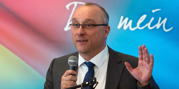 Ein Mann hebt die Hand und spricht in ein Mikrofon Ein Mann hebt die Hand und spricht in ein Mikrofon