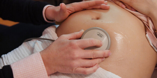 Ein Bauch einer schwangeren Person, auf dem ein medizinisches Gerät (Ultraschall) liegt Ein Bauch einer schwangeren Person, auf dem ein medizinisches Gerät (Ultraschall) liegt