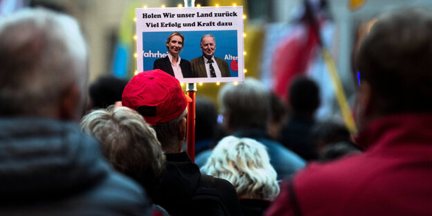 Ein Schild mit "Holen wir unser Land zurück. Viel Erfolg und Kraft dazu" und einem Bild der AfD-Spitzenkandidat*innen ragt aus einer Menschenmasse Ein Schild mit "Holen wir unser Land zurück. Viel Erfolg und Kraft dazu" und einem Bild der AfD-Spitzenkandidat*innen ragt aus einer Menschenmasse