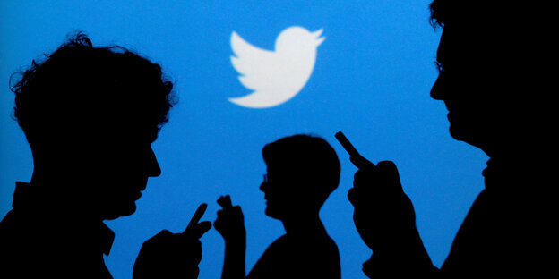 Schatten von Menschen mit Telefon vor dem Twitter-Logo Schatten von Menschen mit Telefon vor dem Twitter-Logo