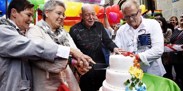 Zwei Frauen und zwei Männer schneiden eine mehrstöckige Torte an