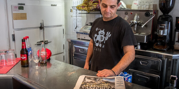 Ein Mann in schwarzem Tshirt schaut auf eine Zeitung, die auf dem Tresen vor ihm liegt Ein Mann in schwarzem Tshirt schaut auf eine Zeitung, die auf dem Tresen vor ihm liegt
