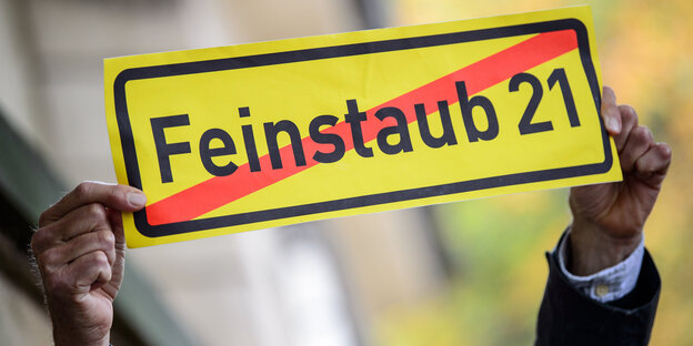 Jemand hält ein Schild hoch, auf dem der durchgestrichene Slogan Feinstaub 21 steht