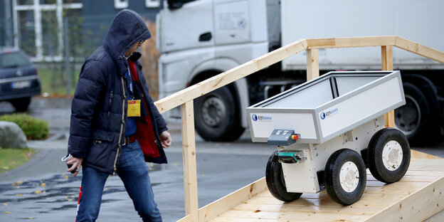 Ein selbstfahrender Roboter folgt einem Mann eine Holzrampe herunter Ein selbstfahrender Roboter folgt einem Mann eine Holzrampe herunter