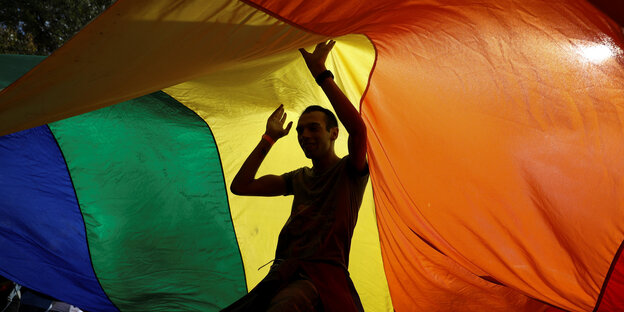 Ein Mann tanzt unter einer Regenbogenflagge Ein Mann tanzt unter einer Regenbogenflagge