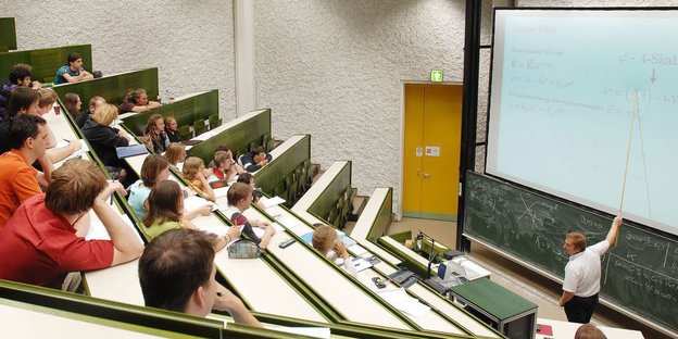 Ein Hörsaal mit Studierenden und ein Dozent an der Tafel vorne. Ein Hörsaal mit Studierenden und ein Dozent an der Tafel vorne.