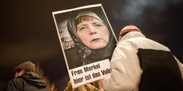 Pegida-Demonstrantin trägt Plakat, das Merkel mit Kopftuch zeigt Pegida-Demonstrantin trägt Plakat, das Merkel mit Kopftuch zeigt
