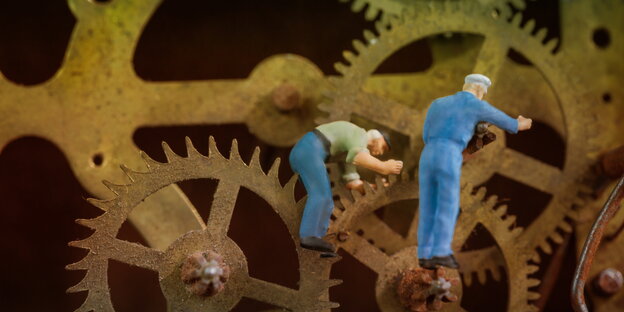 Zwei Miniaturfiguren im Blaumann repaieren ein Uhrwerk Zwei Miniaturfiguren im Blaumann repaieren ein Uhrwerk