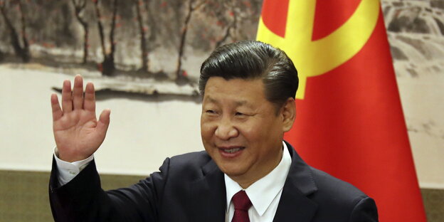 ein Mann mit erhobener rechter Hand, im Hintergrund eine chinesische Fahne ein Mann mit erhobener rechter Hand, im Hintergrund eine chinesische Fahne