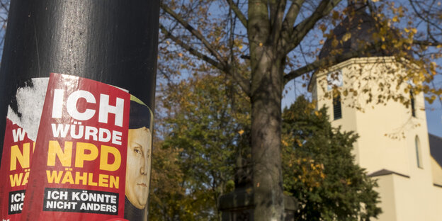 EIn NPD-Sticker klebt auf einer Laterne. Dahinter liegt eine Kirche