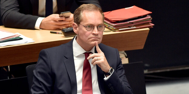 Mann mit Brille sitzt im Anzug im Parlament, kneift das Gesicht zusammen Mann mit Brille sitzt im Anzug im Parlament, kneift das Gesicht zusammen
