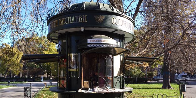 Ein kleiner runder Kiosk in Form einer Litfasssäule steht im herbstlichen Sonnenlicht Ein kleiner runder Kiosk in Form einer Litfasssäule steht im herbstlichen Sonnenlicht