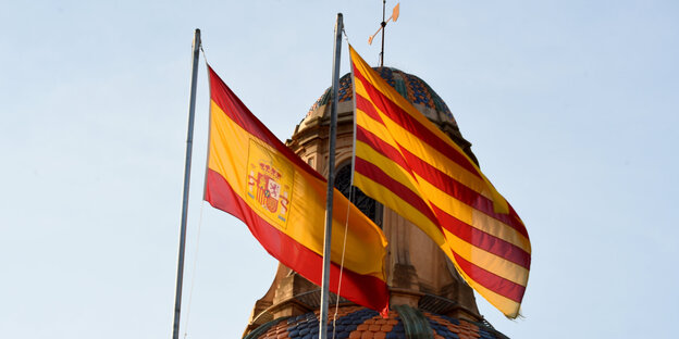 Eine katalanische und eine spanische Flagge flattern vor einer Kuppel im Wind Eine katalanische und eine spanische Flagge flattern vor einer Kuppel im Wind