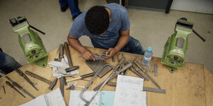Ein junger Mann sitzt vor Werkzeug und Plänen und arbeitet