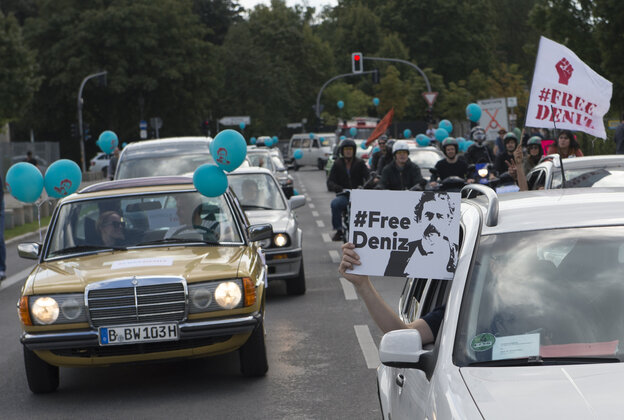 Autos fahren. Menschen halten Ballons und Schilder mit der Aufschrift FreeDeniz aus den Fenstern