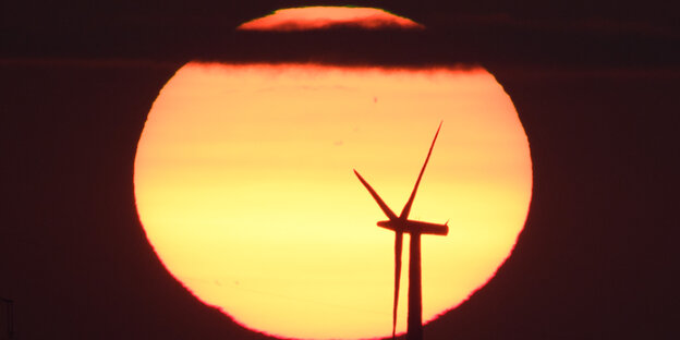 Vor dem hell leuchtenden Mond ist die Silhouette einer Windkraftanlage zu sehen