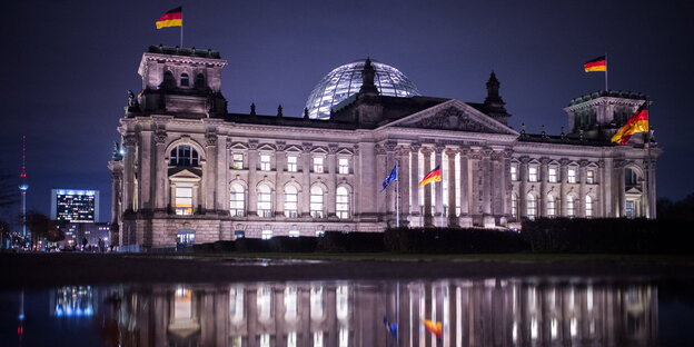 Das Berliner Reichstagsgebäude spiegelt sich am Abend beleuchtet in einer Pfütze Das Berliner Reichstagsgebäude spiegelt sich am Abend beleuchtet in einer Pfütze