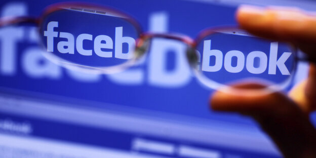 Eine Brille wird vor einem Bildschirm mit Facebooklogo gehalten Eine Brille wird vor einem Bildschirm mit Facebooklogo gehalten