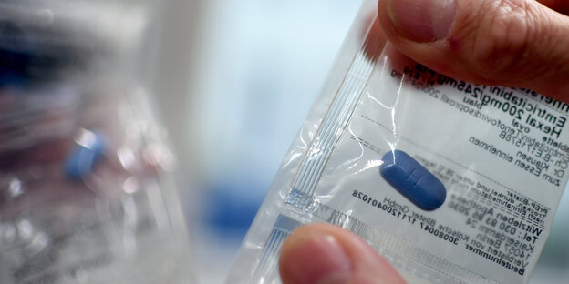 Eine Hand hält eine Plastikhülle, in der eine Pille steckt Eine Hand hält eine Plastikhülle, in der eine Pille steckt