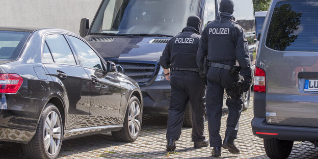 Zwei Polizisten laufen zwischen zwei Autos umher Zwei Polizisten laufen zwischen zwei Autos umher