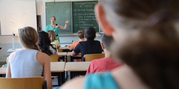 Eine Lehrerin steht an der Tafel und wendet sich ihrer Klasse zu Eine Lehrerin steht an der Tafel und wendet sich ihrer Klasse zu